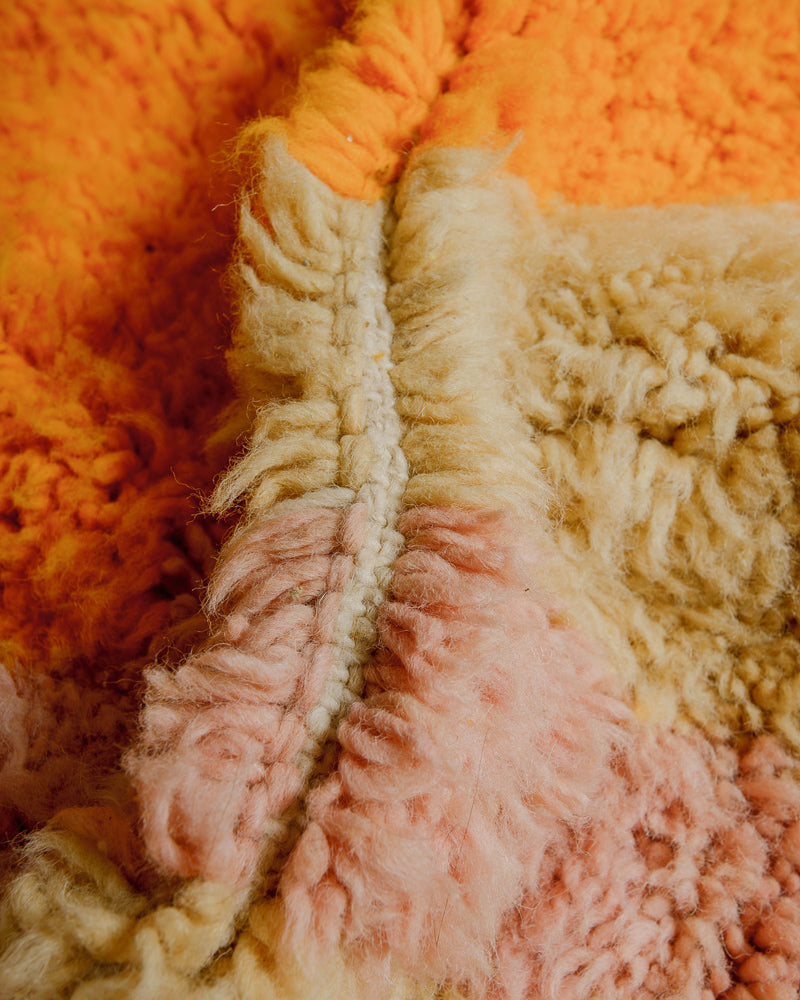 Close up of fluffy wool rug in orange, faded yellow and rose. 