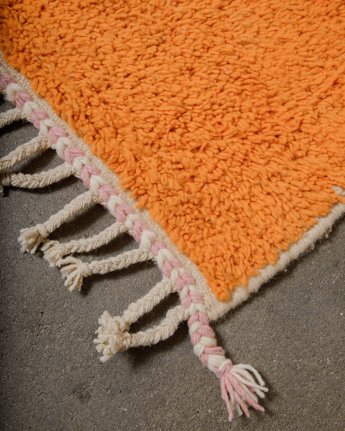 Corner of rug made of fluffy orange wool with natural wool tassels. 