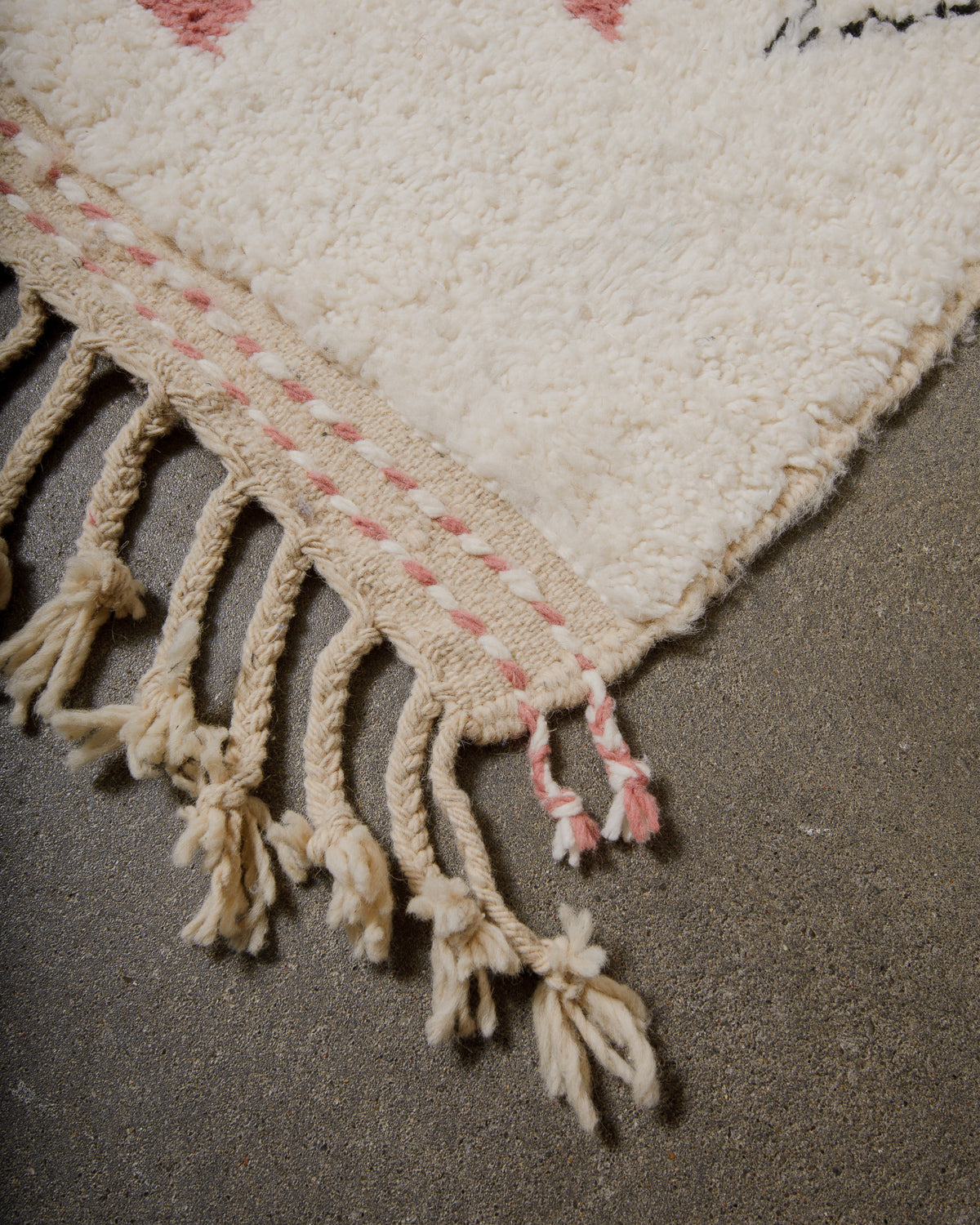 Corner of wool rug with tassels on concrete floor. 