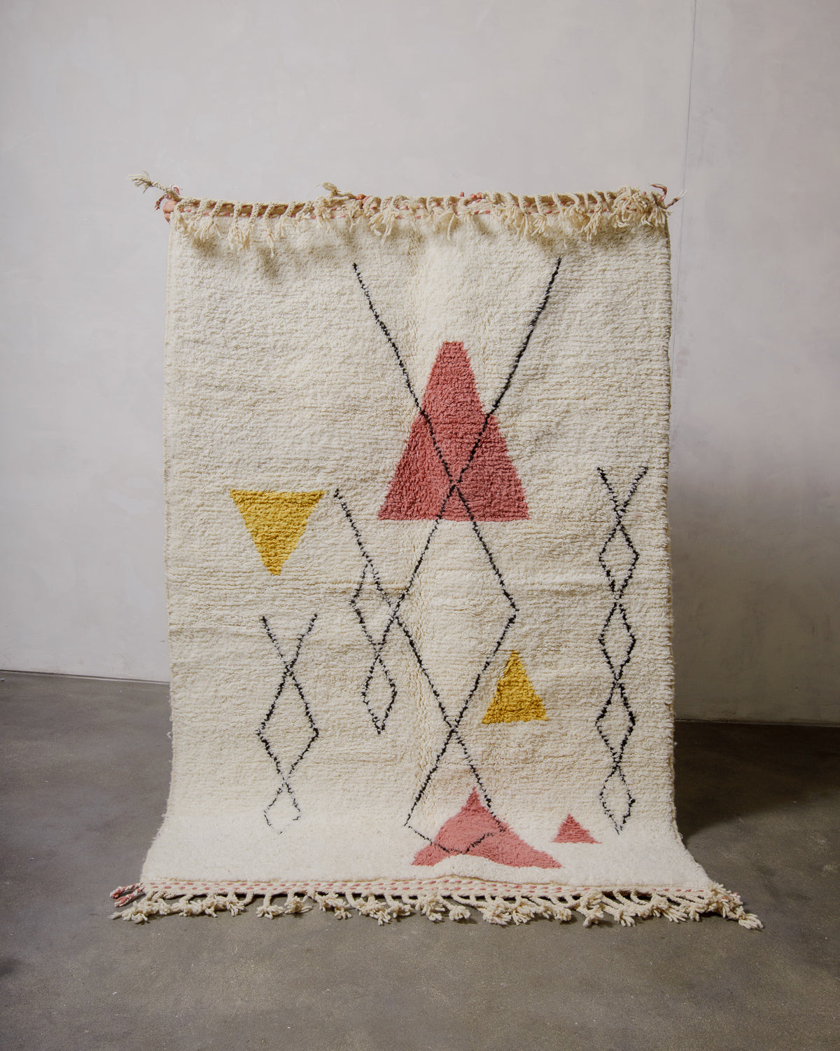 Cream rug with abstract geometric design being held up in front of a white wall. 