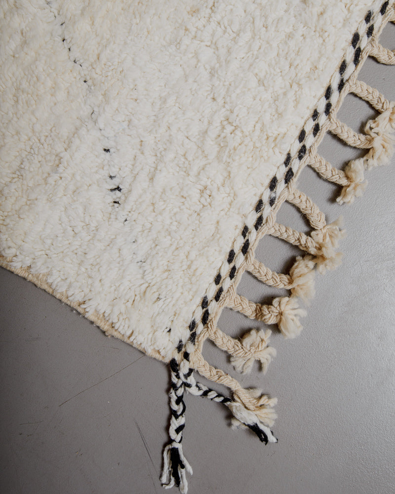 Corner of wool rug with natural wool tassels and black details along the edge.