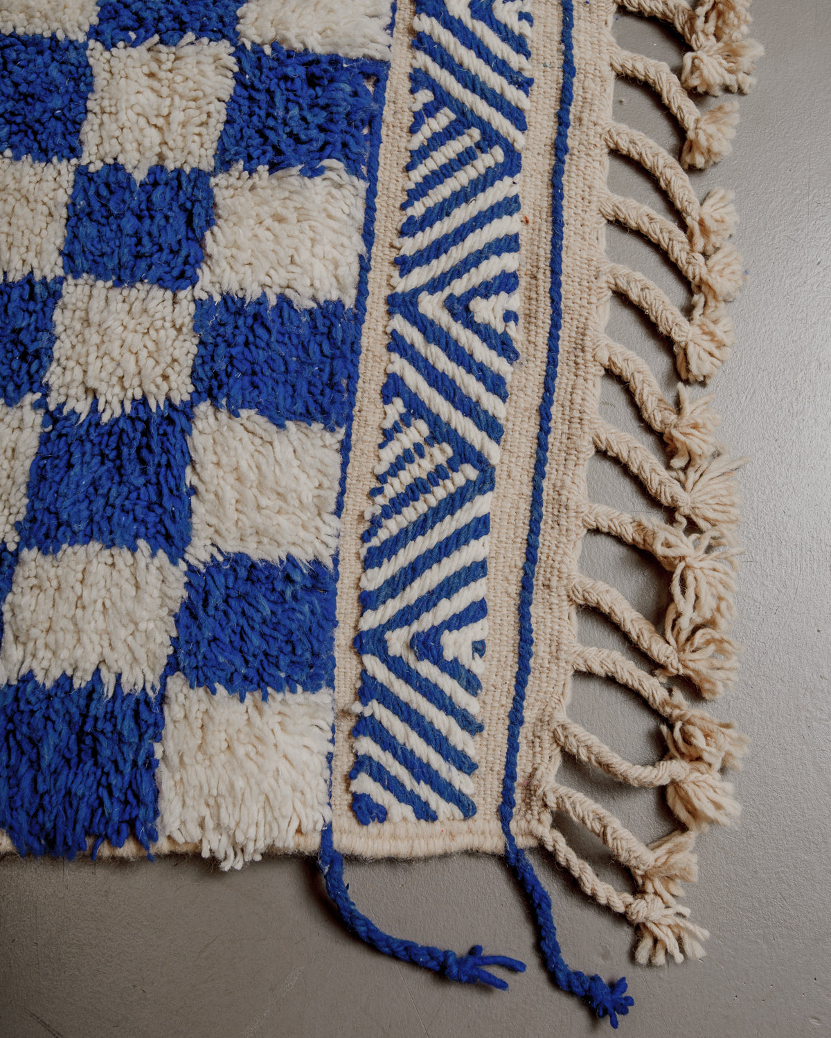 Corner of Berber rug showing embroidered pattern and natural wool tassels. 