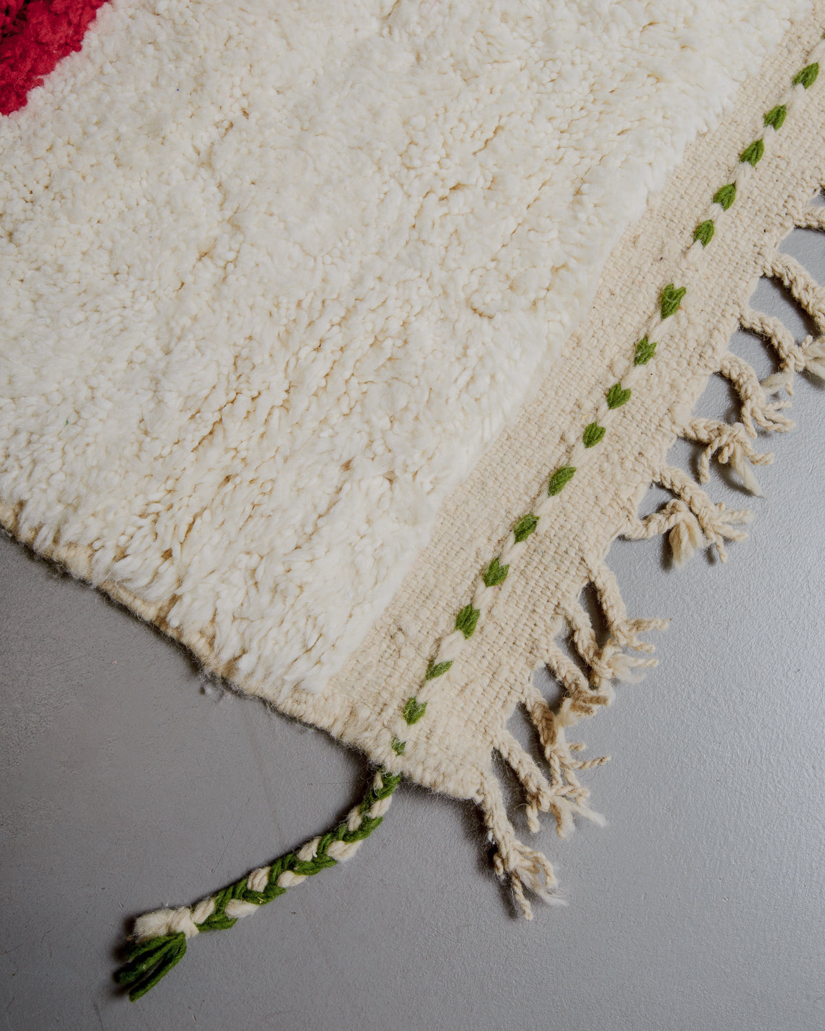 Corner of rug with natural wool tassels and green woven into the end.