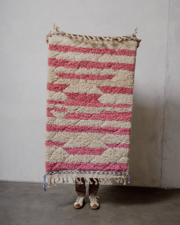 Person holding a pink and cream striped rug against a plain wall.