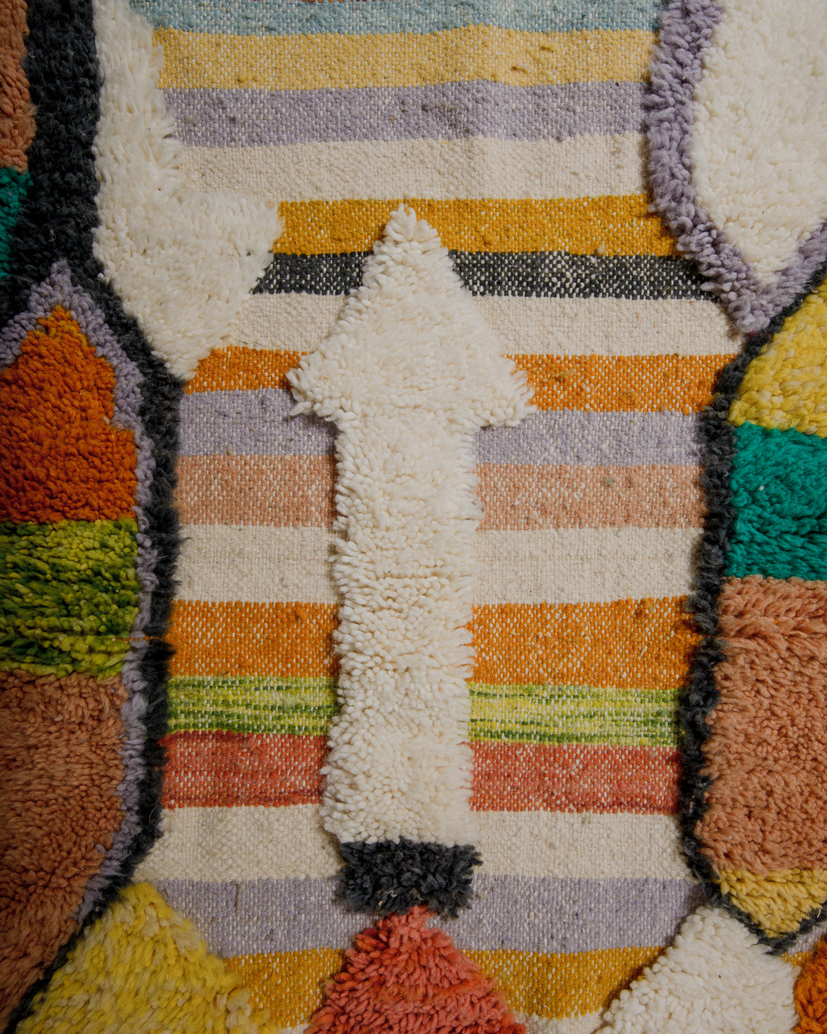 Close-up of a textured rug with multicolored stripes and fluffy arrow form.