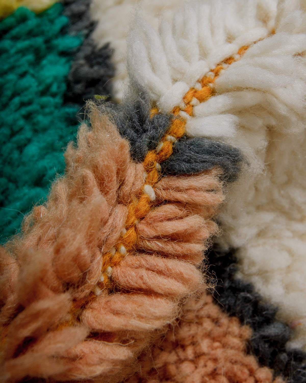 Close-up of a textured wool rug with fluffy pile in rust, grey, teal and cream.