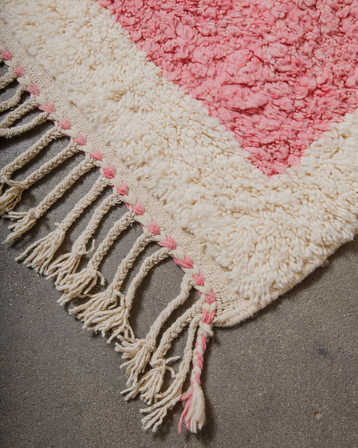 Close-up of a textured wool rug with pink and cream colours and fringes.