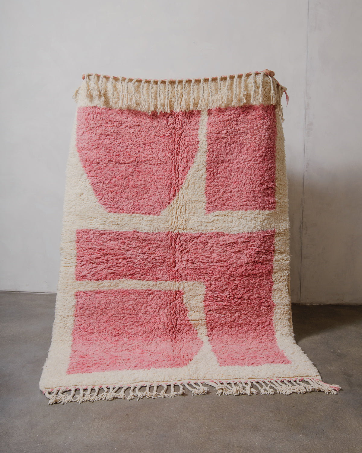 Pink and white wool Beniourain rug with fringes on a plain background.