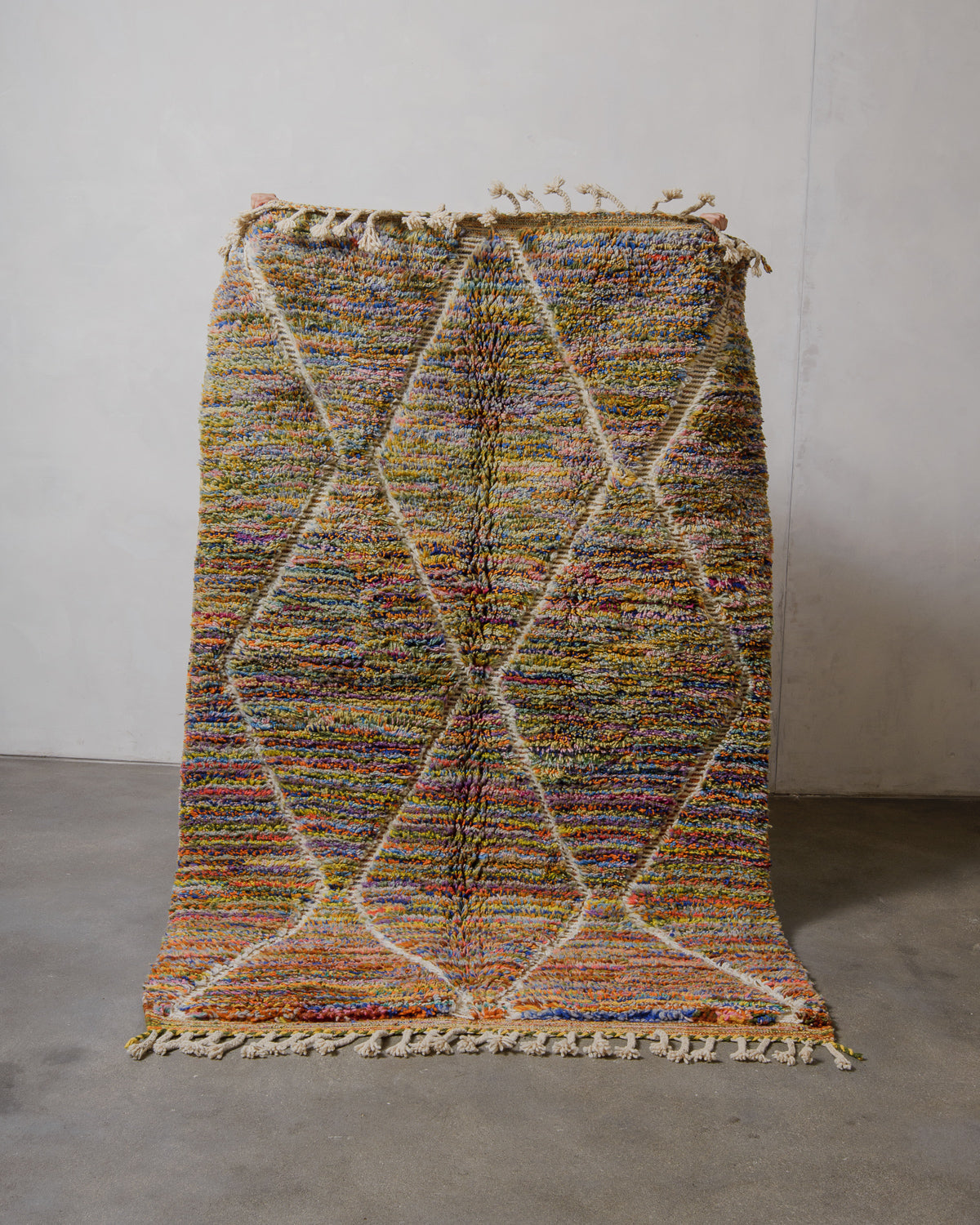 Multicolored wool rug on a plain floor with a white wall background.