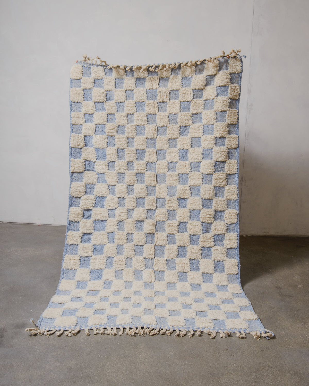 Checkered rug with blue and beige squares on a plain background