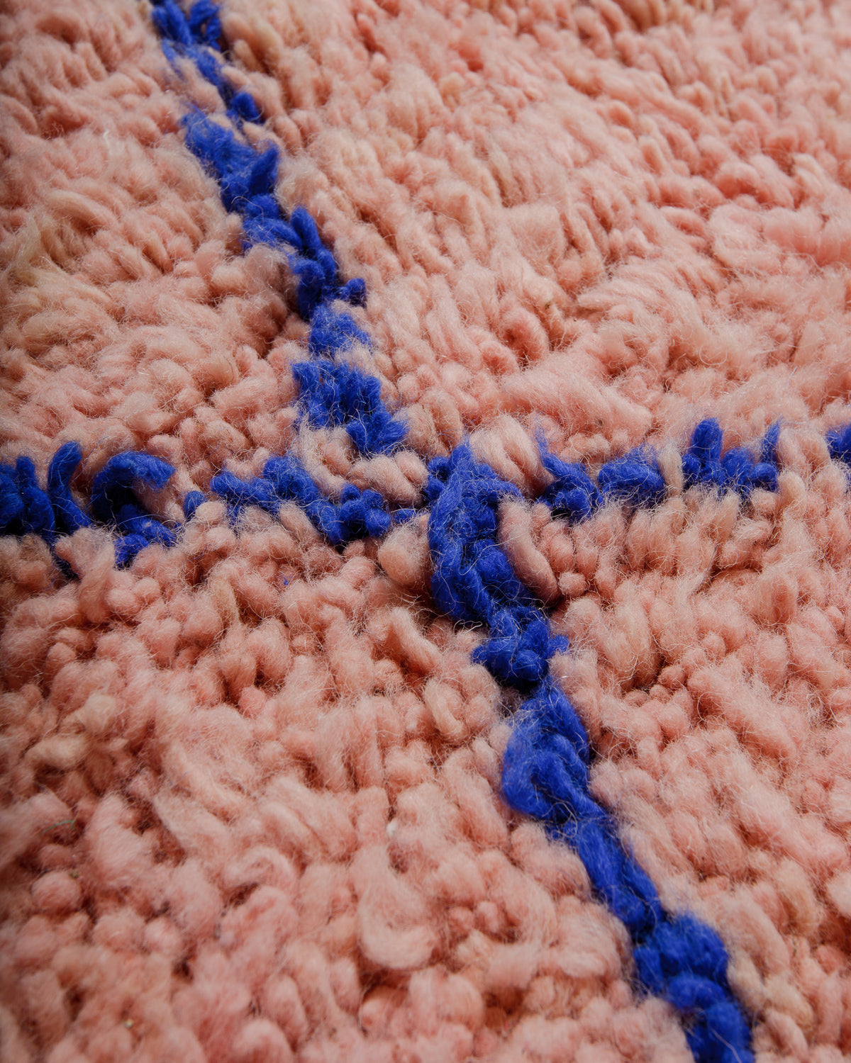 Close up of the surface of a fluffy wool rug in soft pink and dark blue.