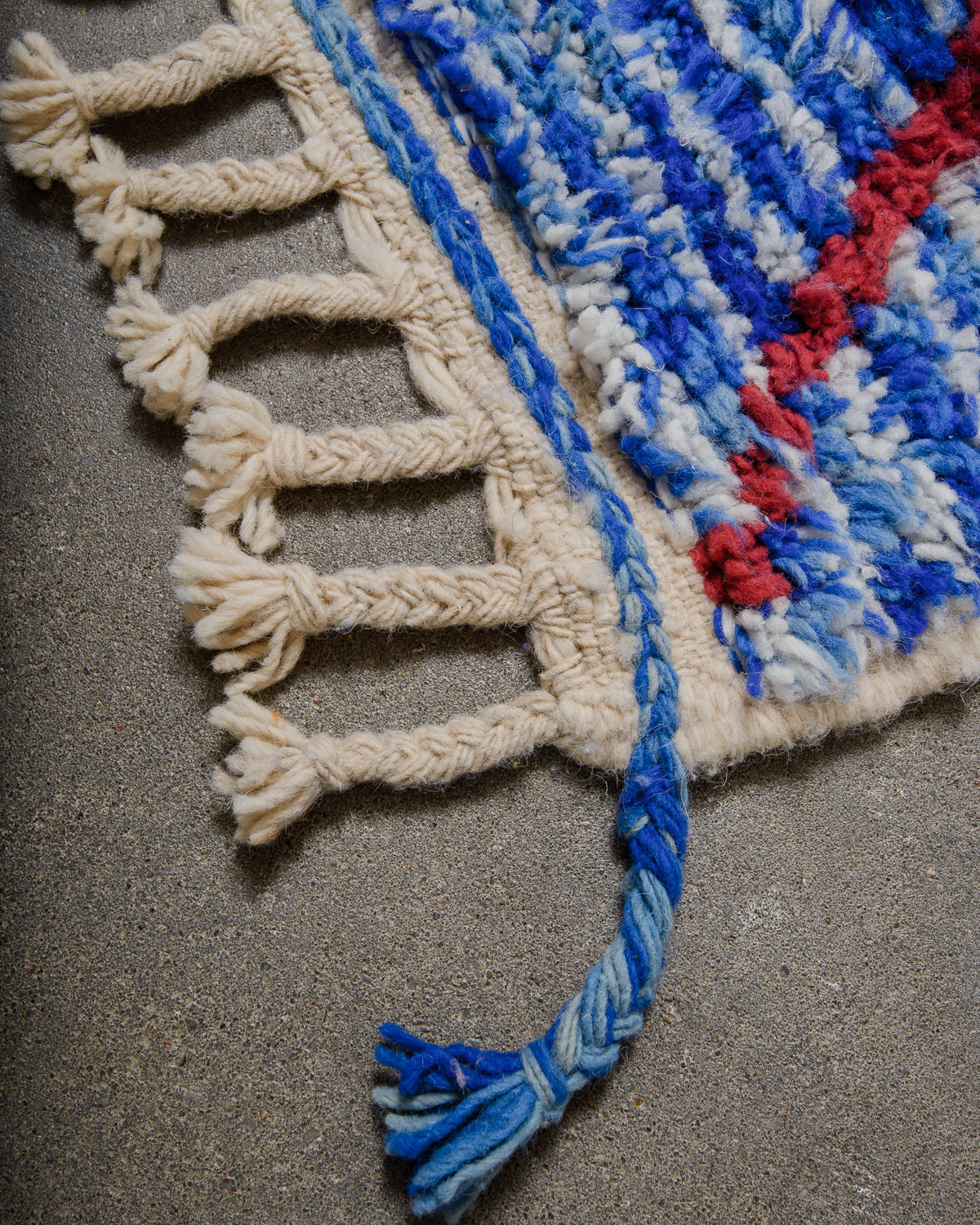 Corner of blue wool rug with natural wool tassels on concrete floor. 