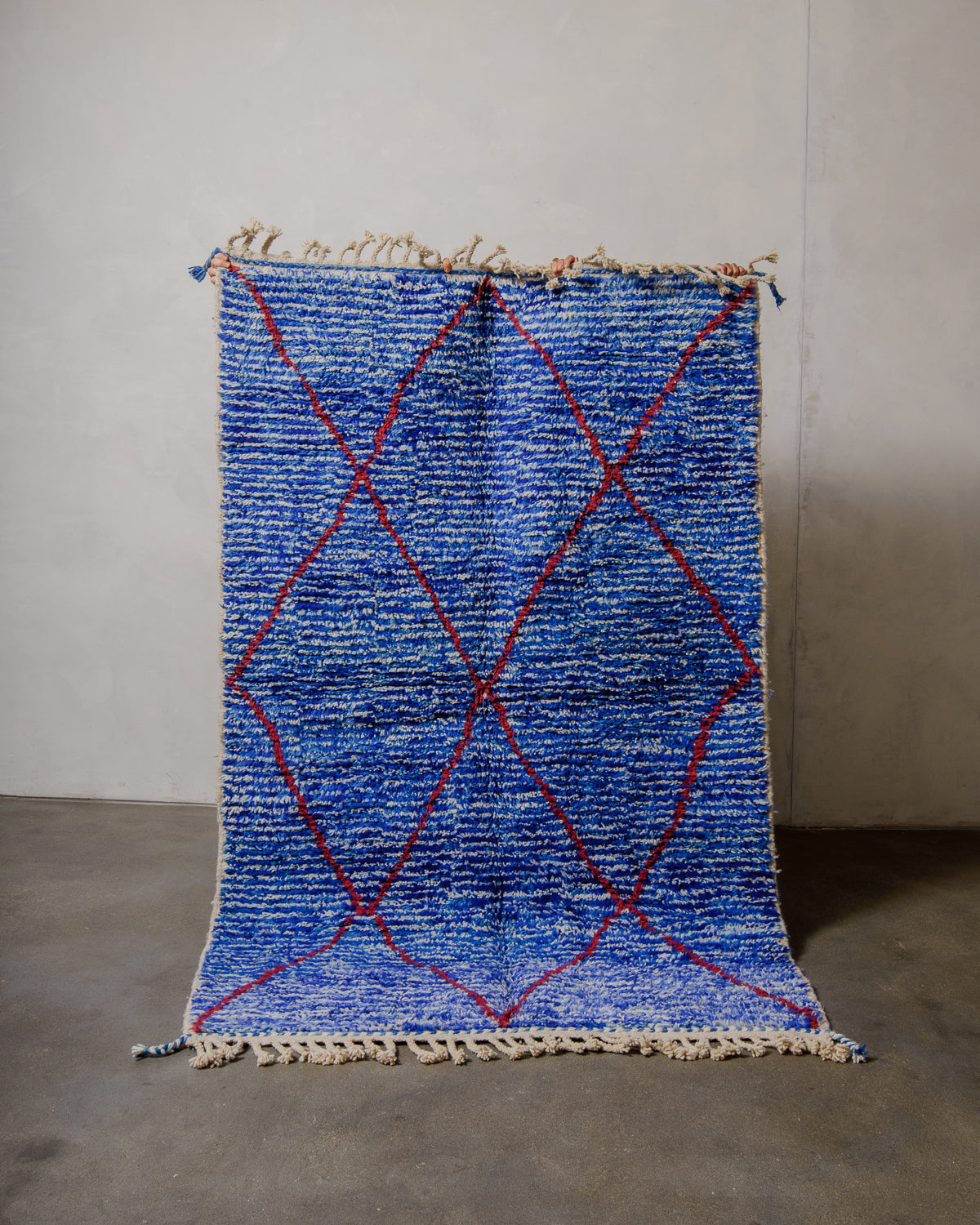Berberlin special edition rug in blue being held up in front of a plain wall. 