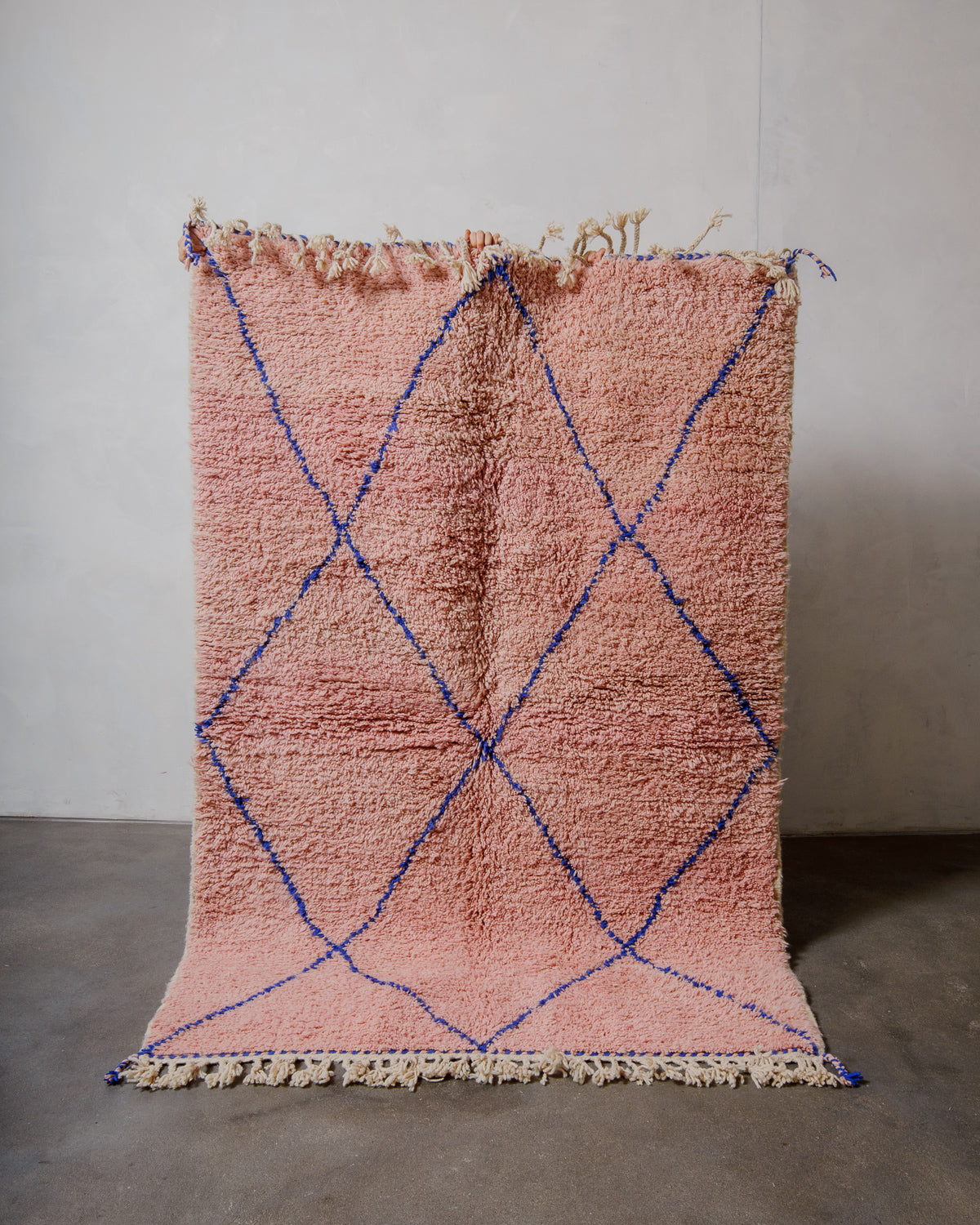 Berberlin beniourain in soft rose with a dark blue diamond pattern, being held in front of a plain wall. 