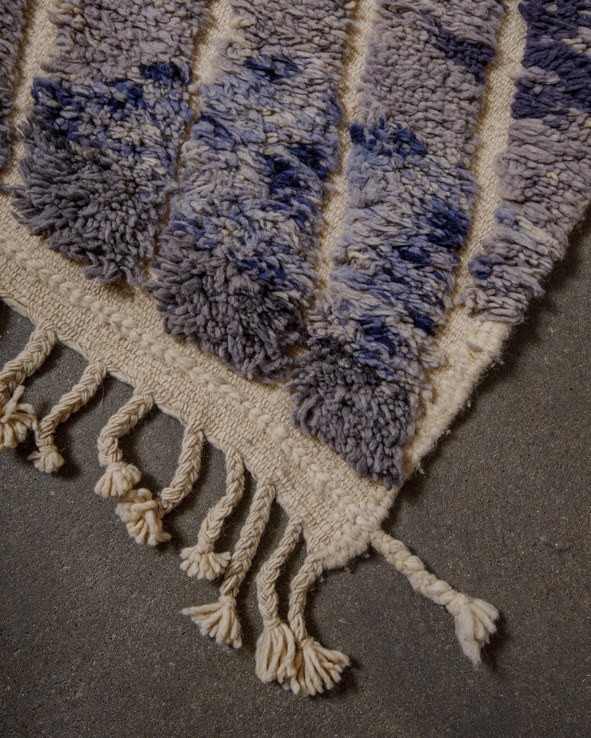 Corner of wool rug with tassels on concrete floor. 