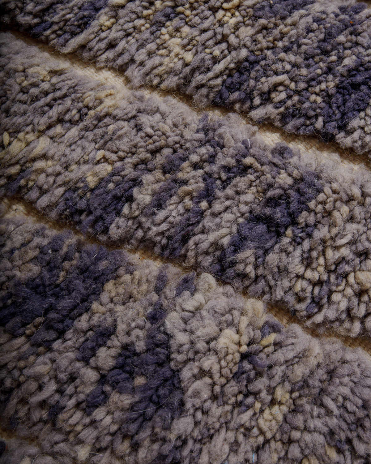Close up of surface of wool rug in shades of purple. grey and cream.