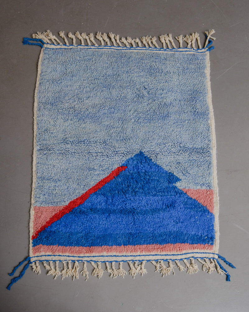 Berberlin beniourain rug in shades of blue, red and pink on grey floor.