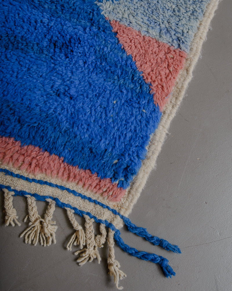 Corner of wool rug with natural wool tassels on grey floor. 