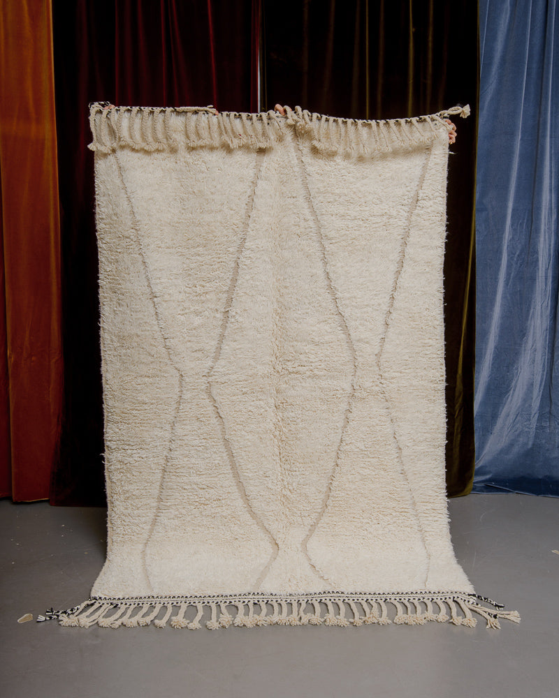 Cream beniourain rug being held up in front of velvet curtains