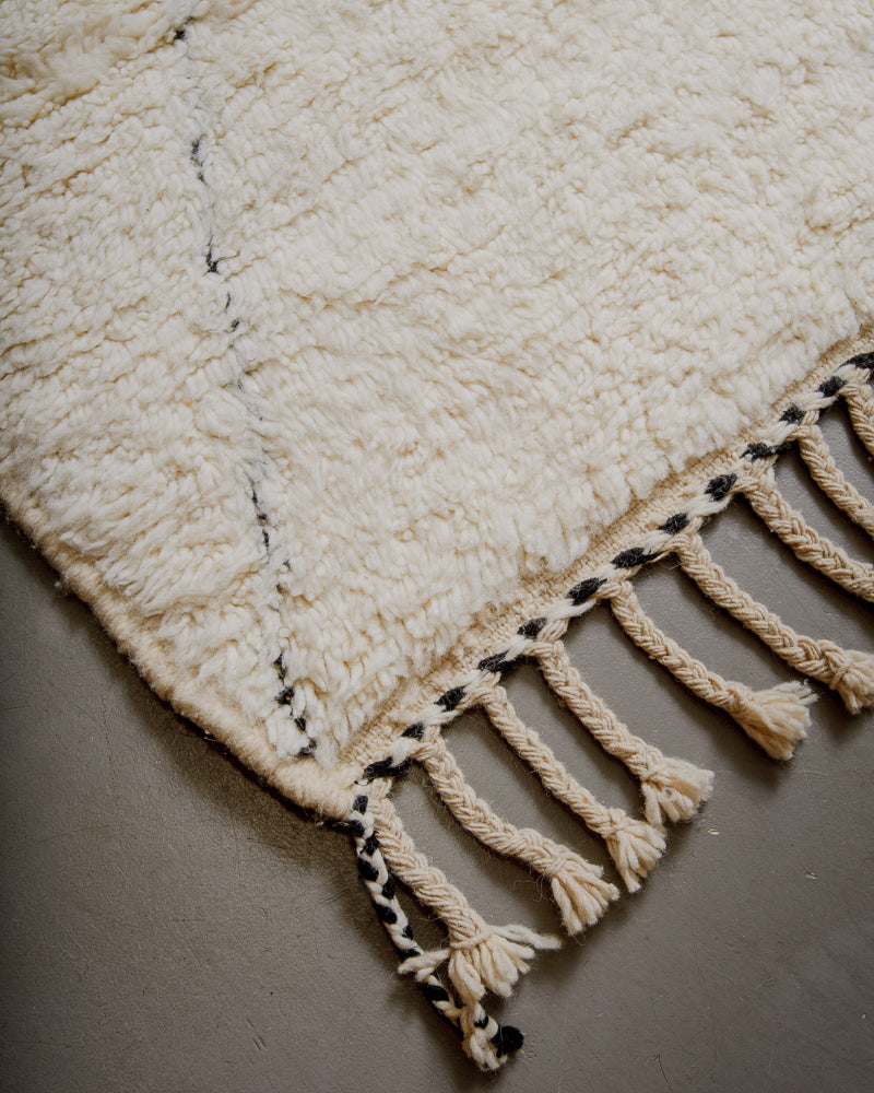 Corner of cream Berberlin beniourain with black lines and natural wool tassels.
