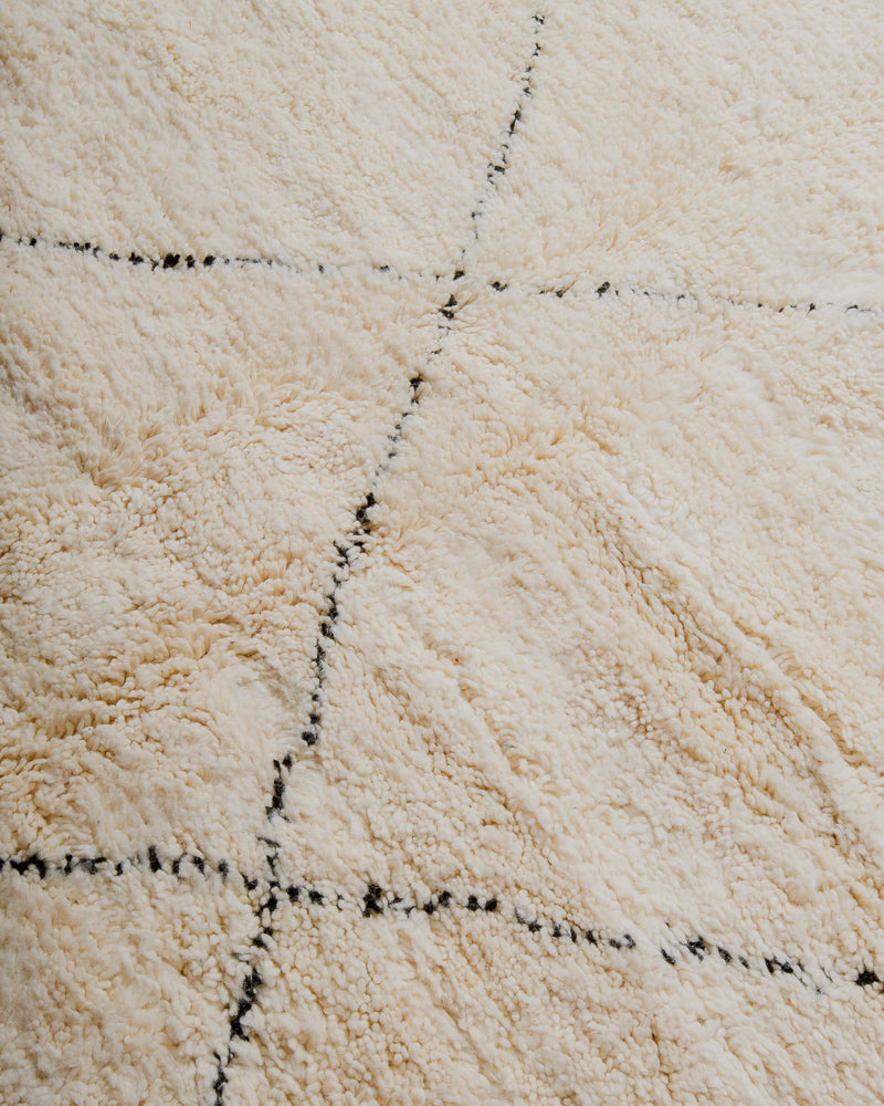 Close up of surface of cream wool rug with black lines.