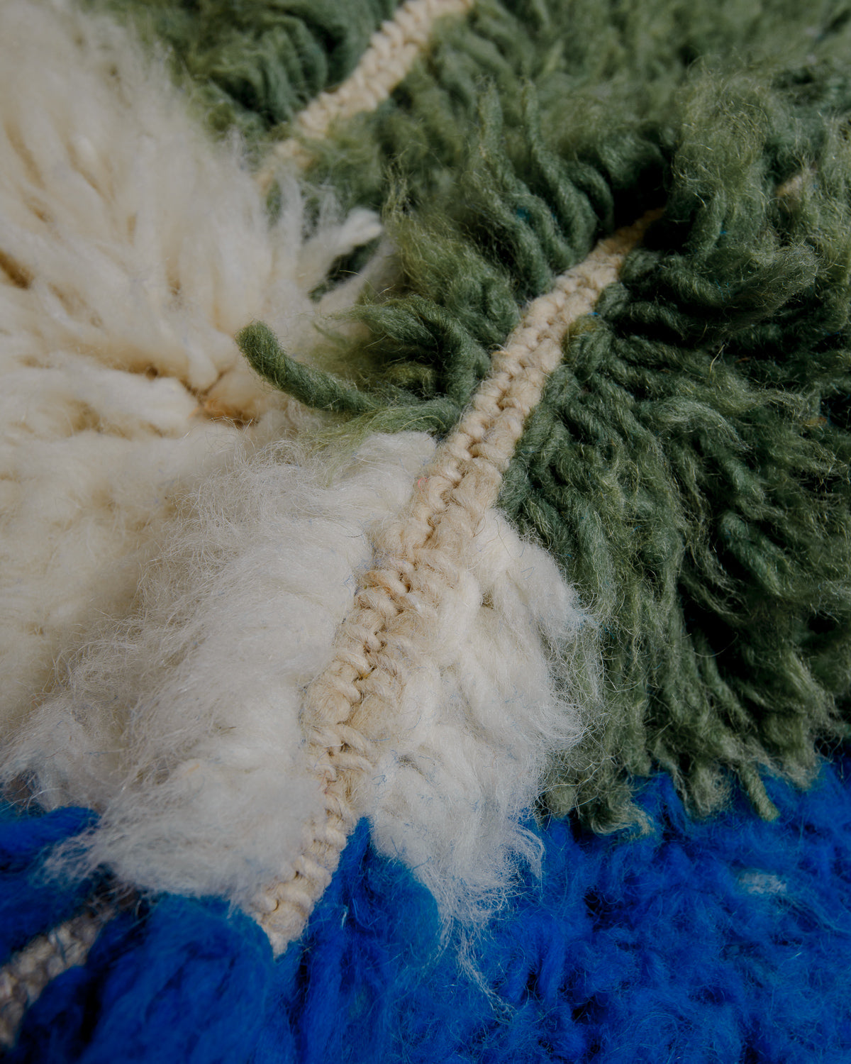 Close up showing cream, olive green and blue coloured wool with a soft, fluffy texture.