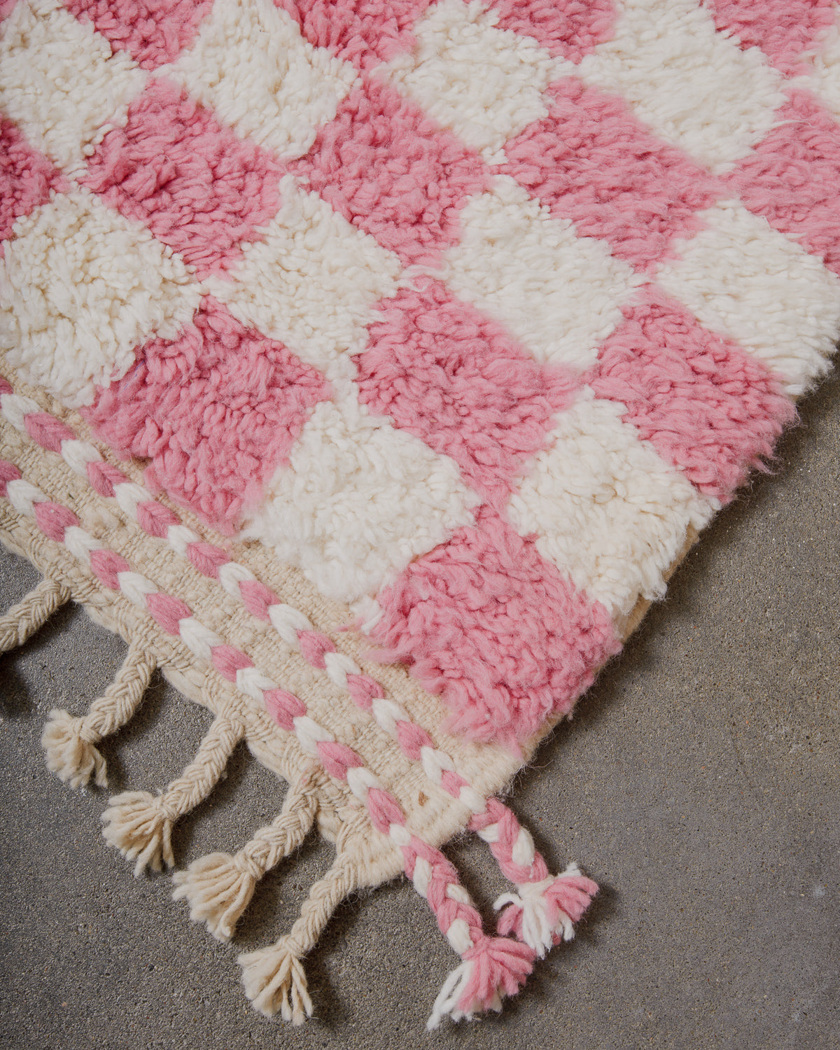Pink and white checkered rug with tassels on a gray surface