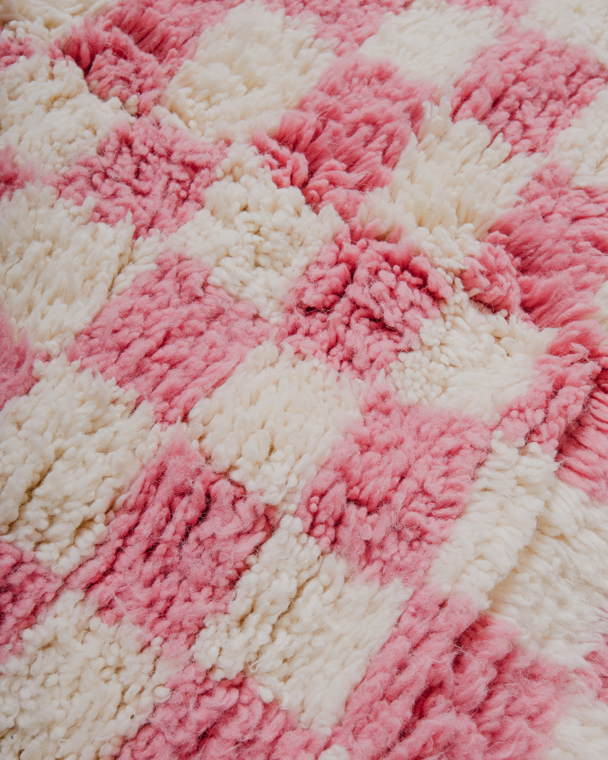 Surface of a pink and white textured rug with a checkered pattern.