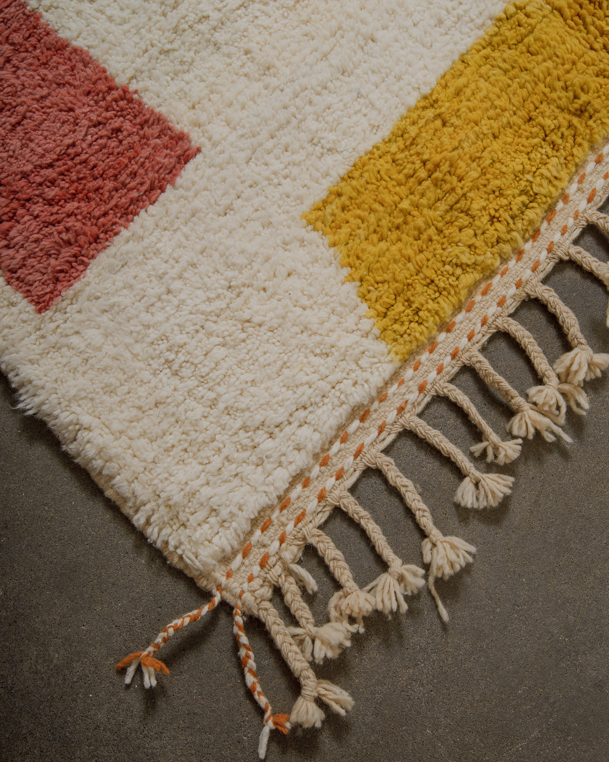 Corner of a textured rug with geometric pattern and tassels on a dark surface