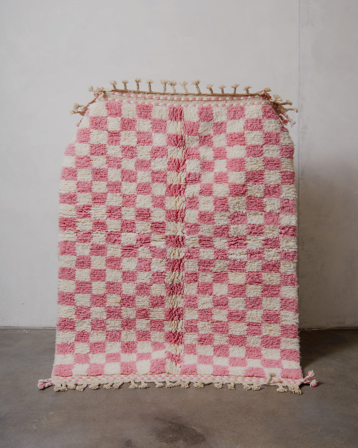 Pink and white checkered rug with tassels on a plain background