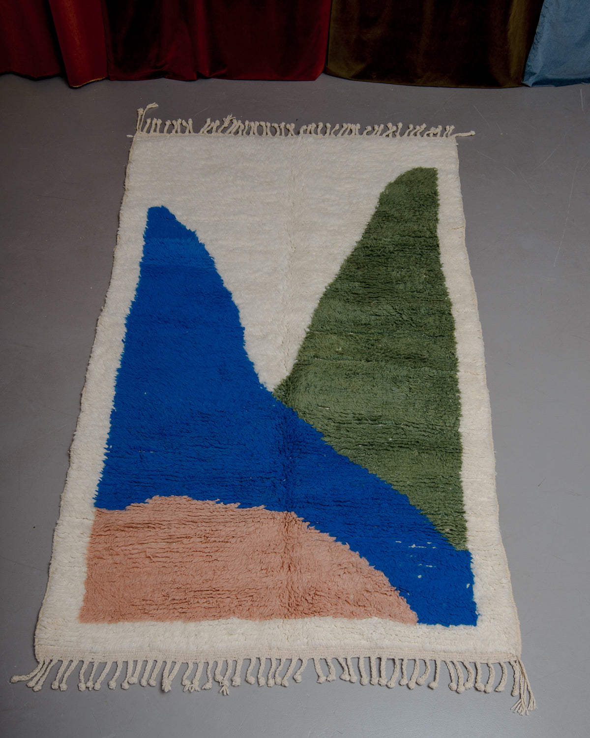Berberlin beniouran rug in cream with colourful forms laying on a grey floor in front of velvet curtains