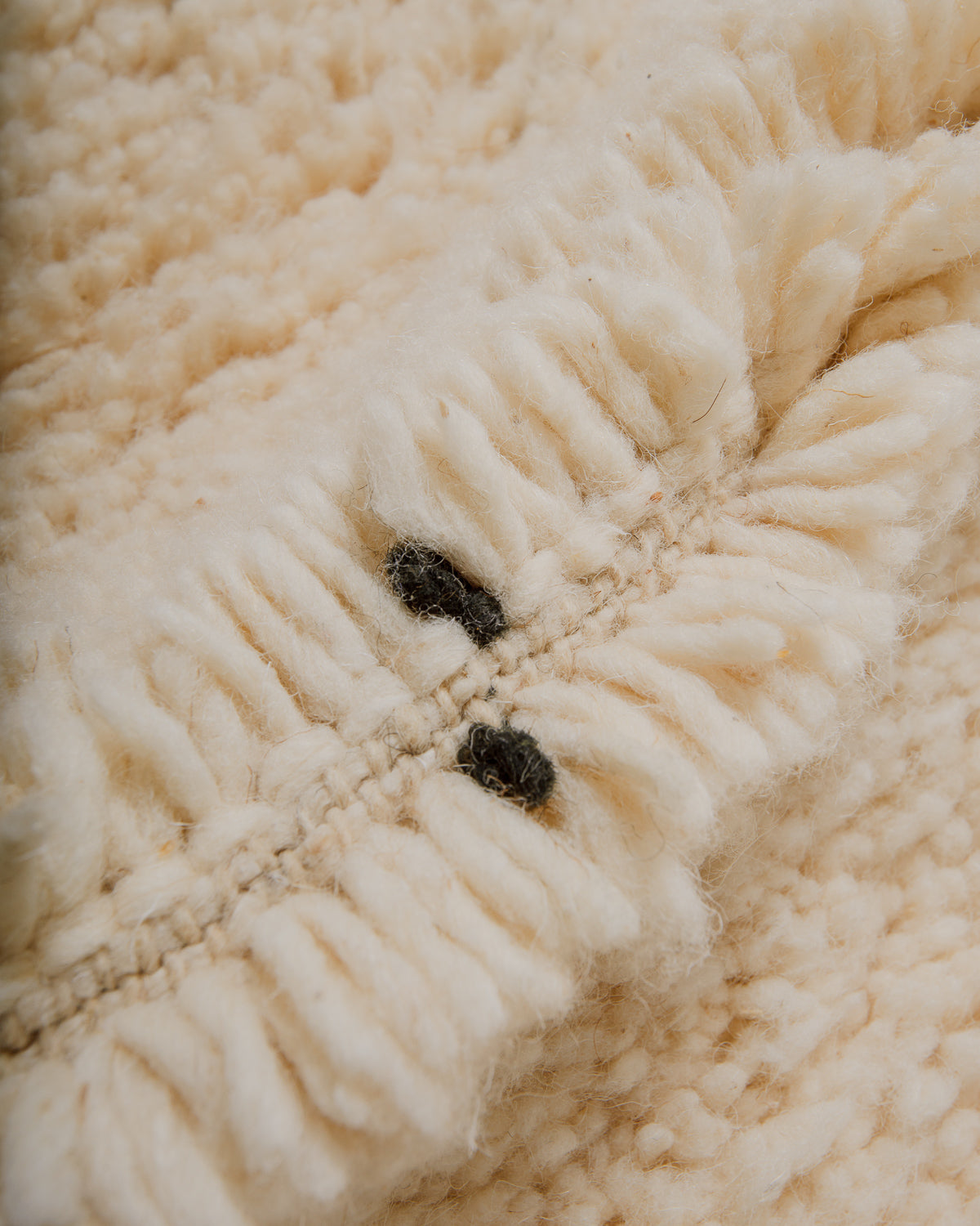 Close-up of cream wool rug showing the shorter black threads that make up the diamond design.