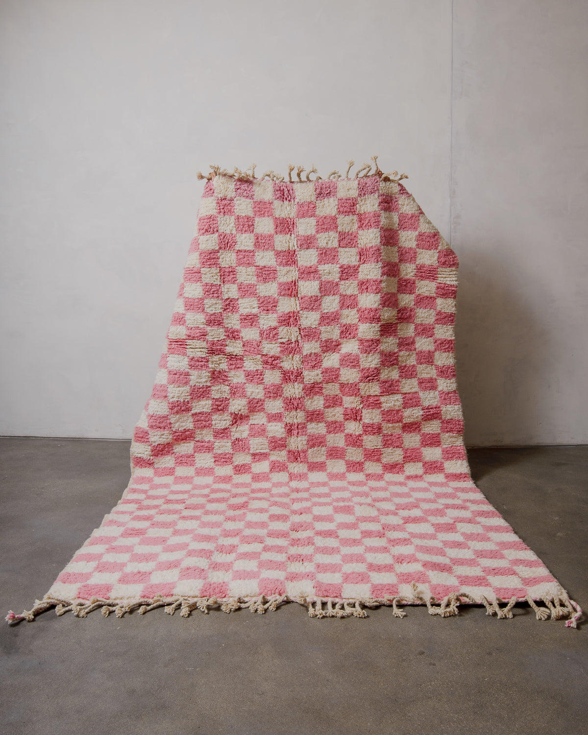 Berberlin rug with pink and cream checkered pattern held up in front of plain background. 