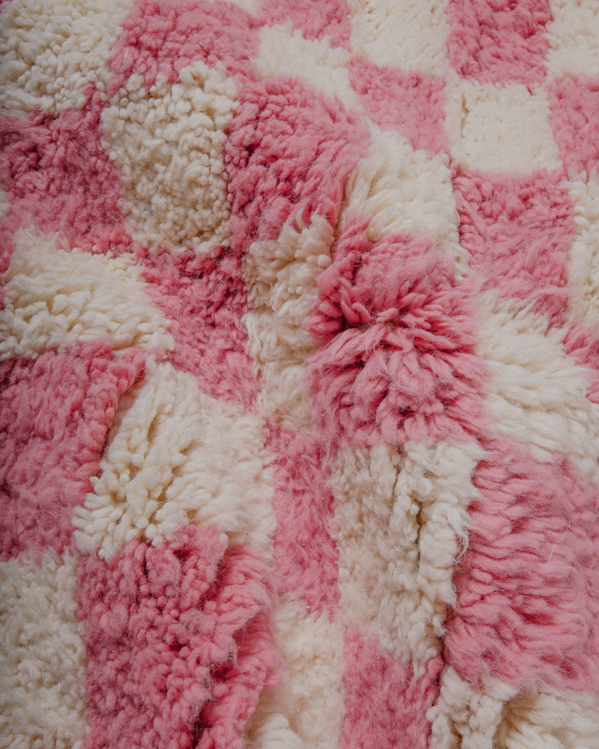 close up of surface of pink and cream checkered wool beniourain rug. 