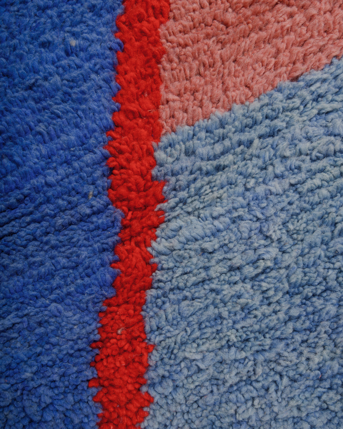 Close up of surface of modern rug in shades of blue, pink and red.