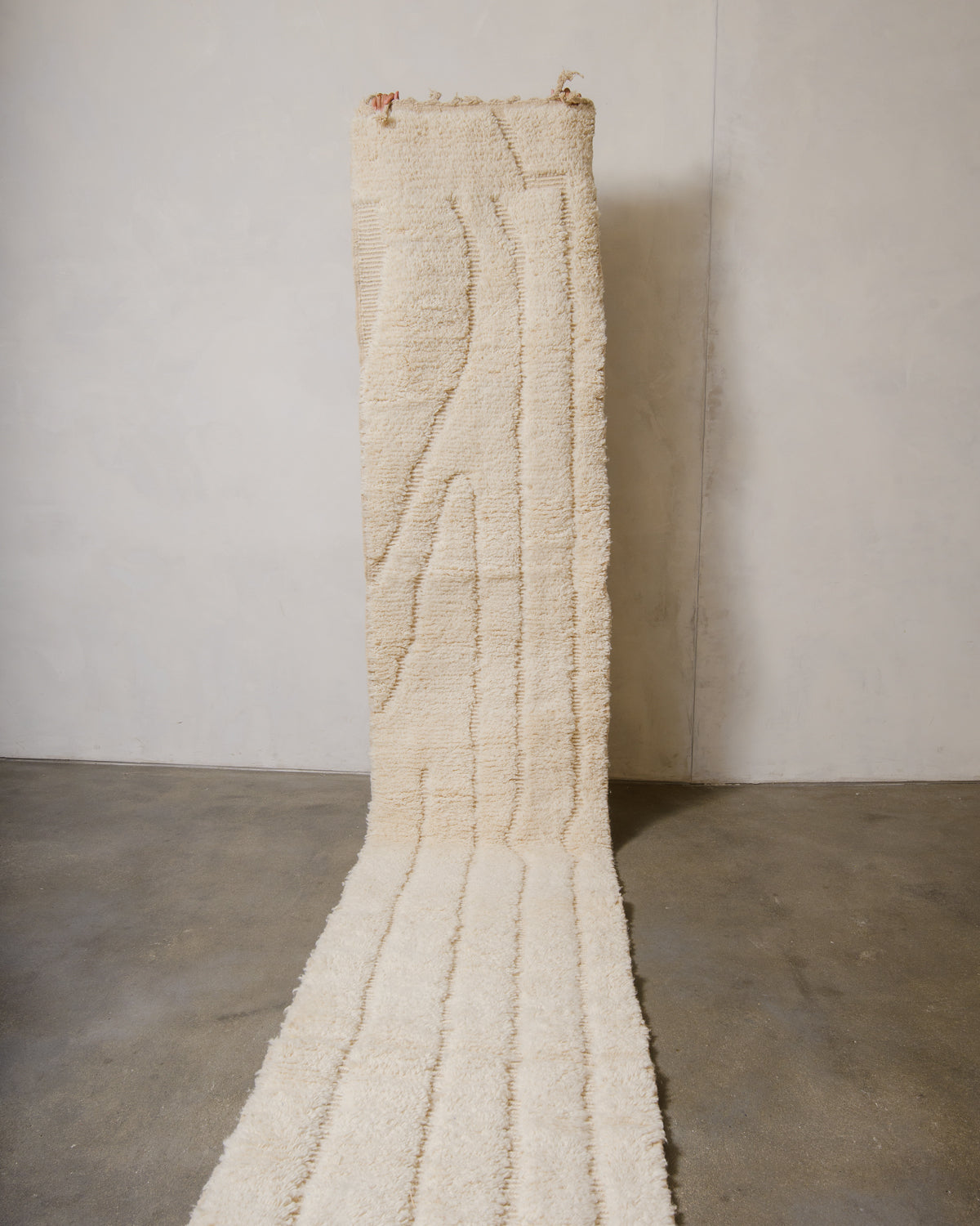 Berberlin Berber runner rug in soft cream wool, being held up in front of a white wall. 