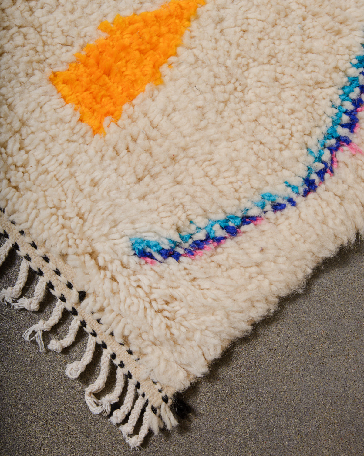 Corner of Azilal run with cream wool and white cotton tassels and black and cream weaving across the edge.