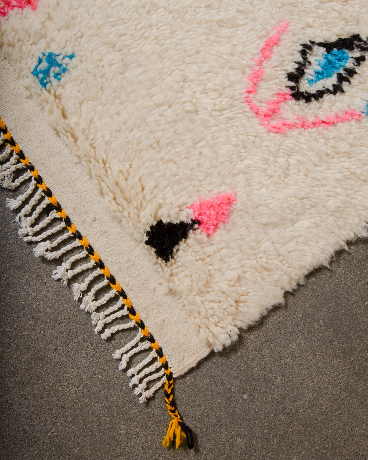 Corner of Azilal run with cream wool and colourful design and white cotton tassels across the edge with black and yellow trim.