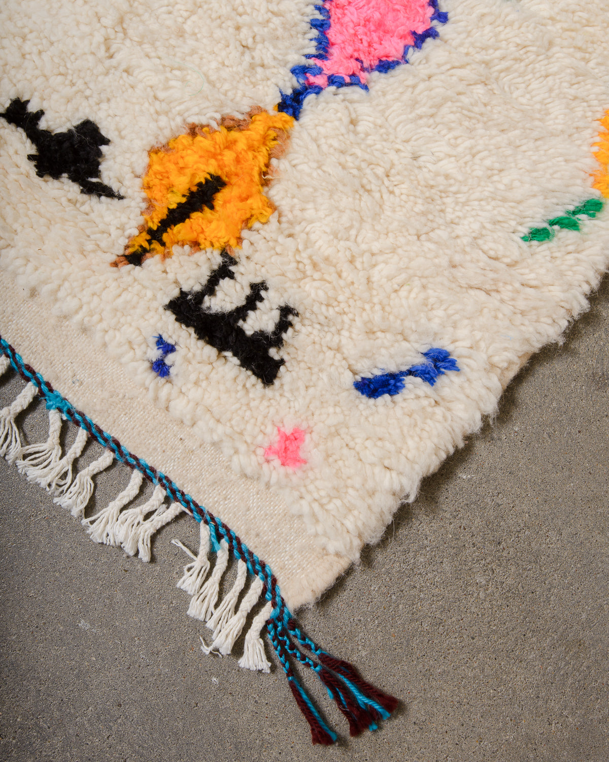 Corner of Azilal rug with a tightly woven edge and white cotton tassels along the end.