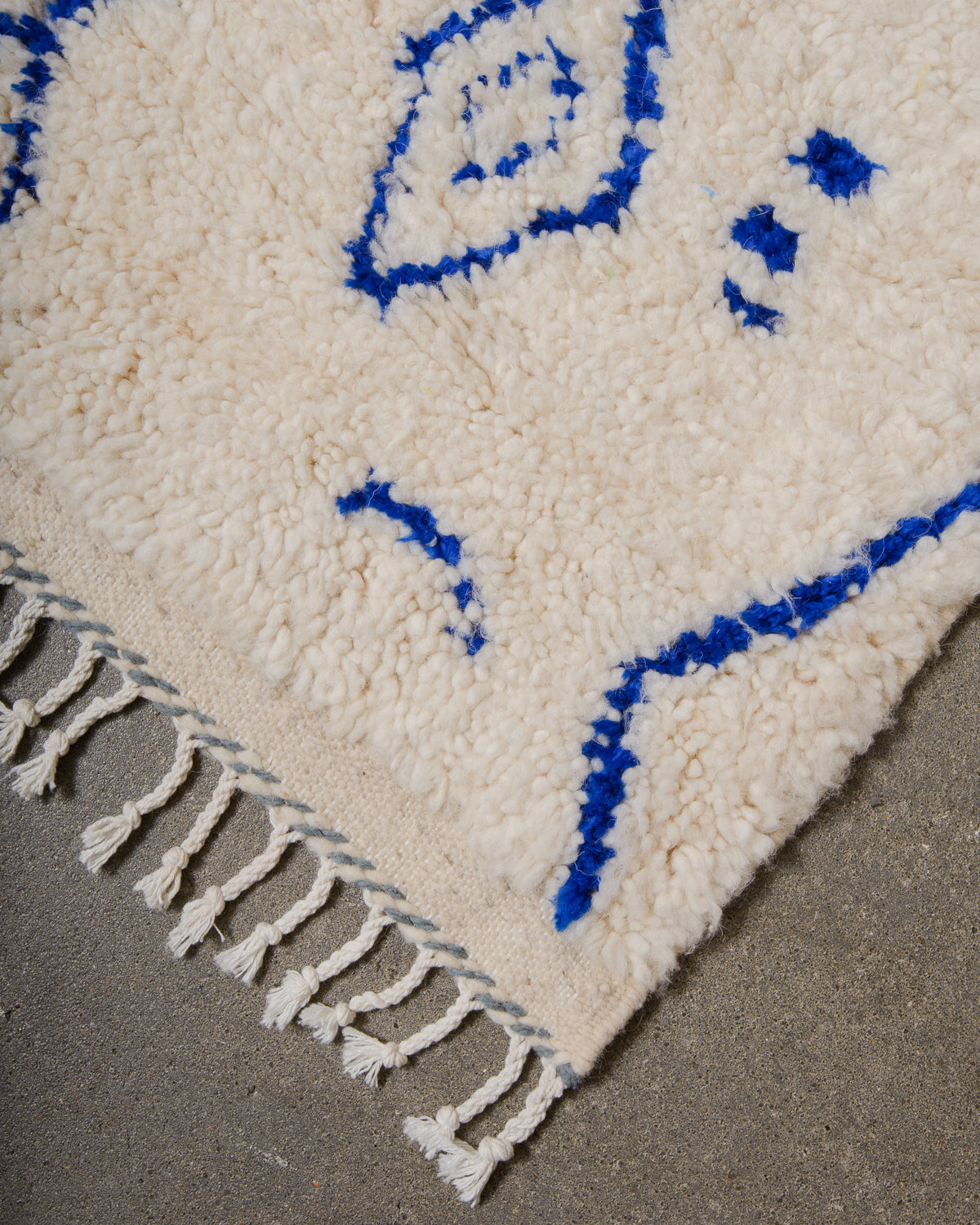 Corner of Azilal rug with a tightly woven edge and white cotton tassels along the end.