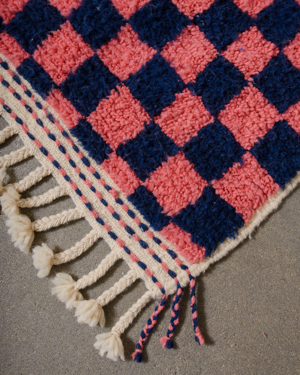 Corner of wool berber rug that is finished with tightly woven ends and natural wool tassels across the ends.