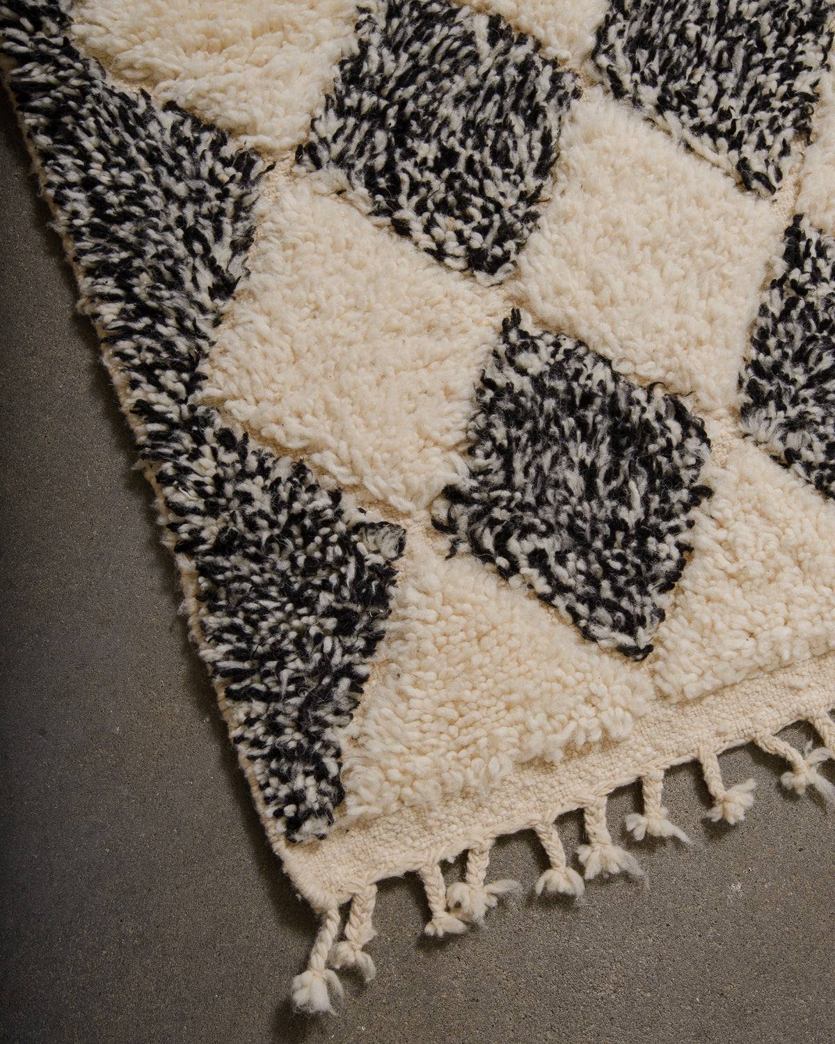 Corner of wool berber rug that is finished with tightly woven ends and natural wool tassels across the ends.
