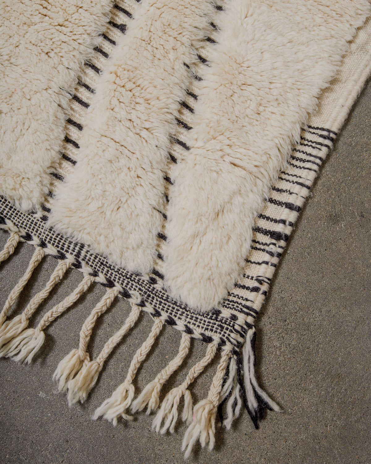 Textured rug with black and white pattern and tassels on a gray surface