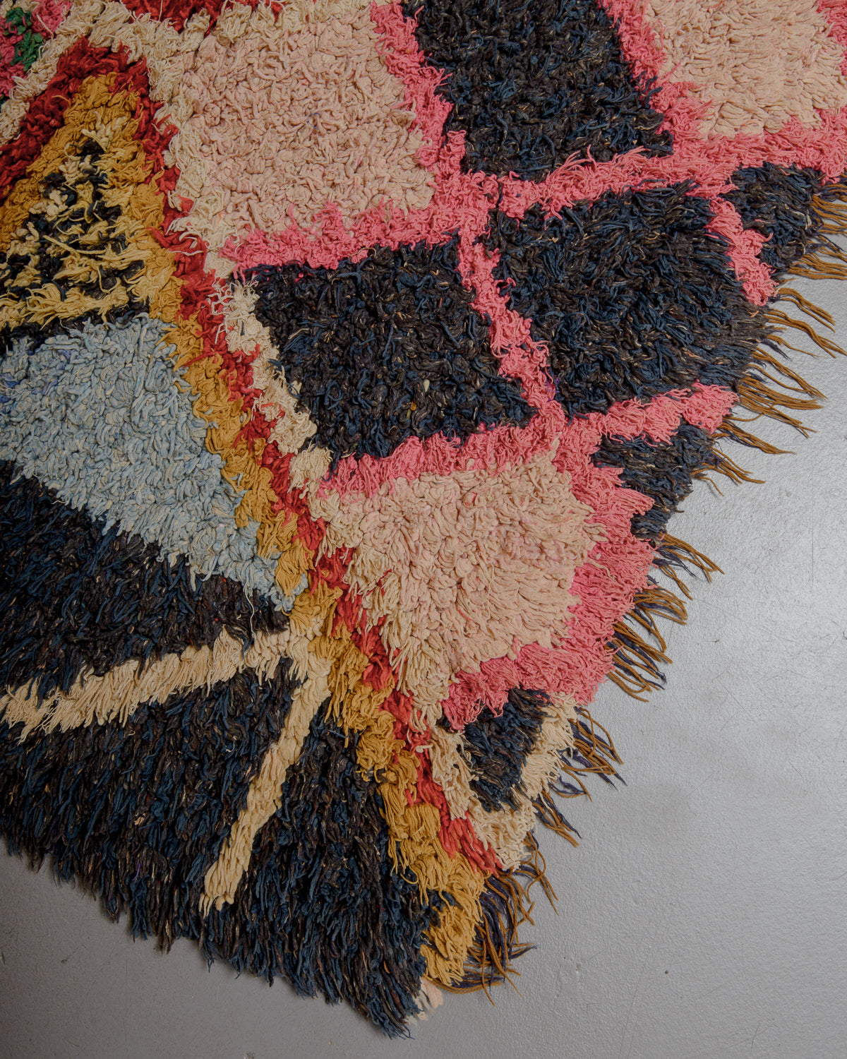 Corner of boucherouite rug on grey floor.