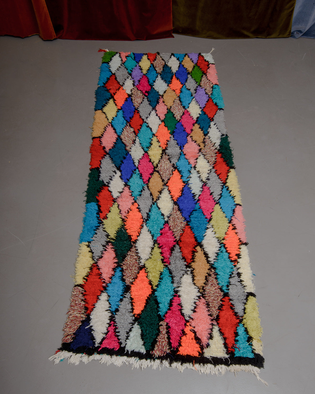 Vintage Berberlin boucherouite runner rug on grey floor in front of velvet curtain. 
