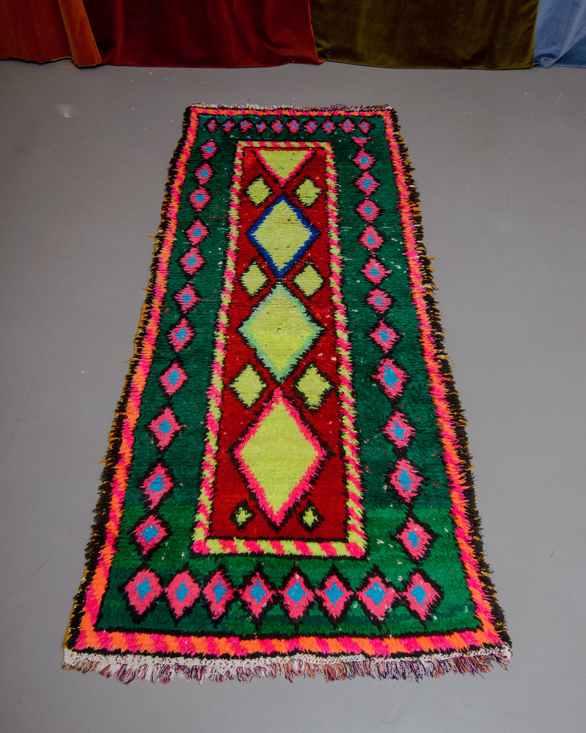 Vintage Berberlin boucherouite runner rug on grey floor in front of velvet curtain. 