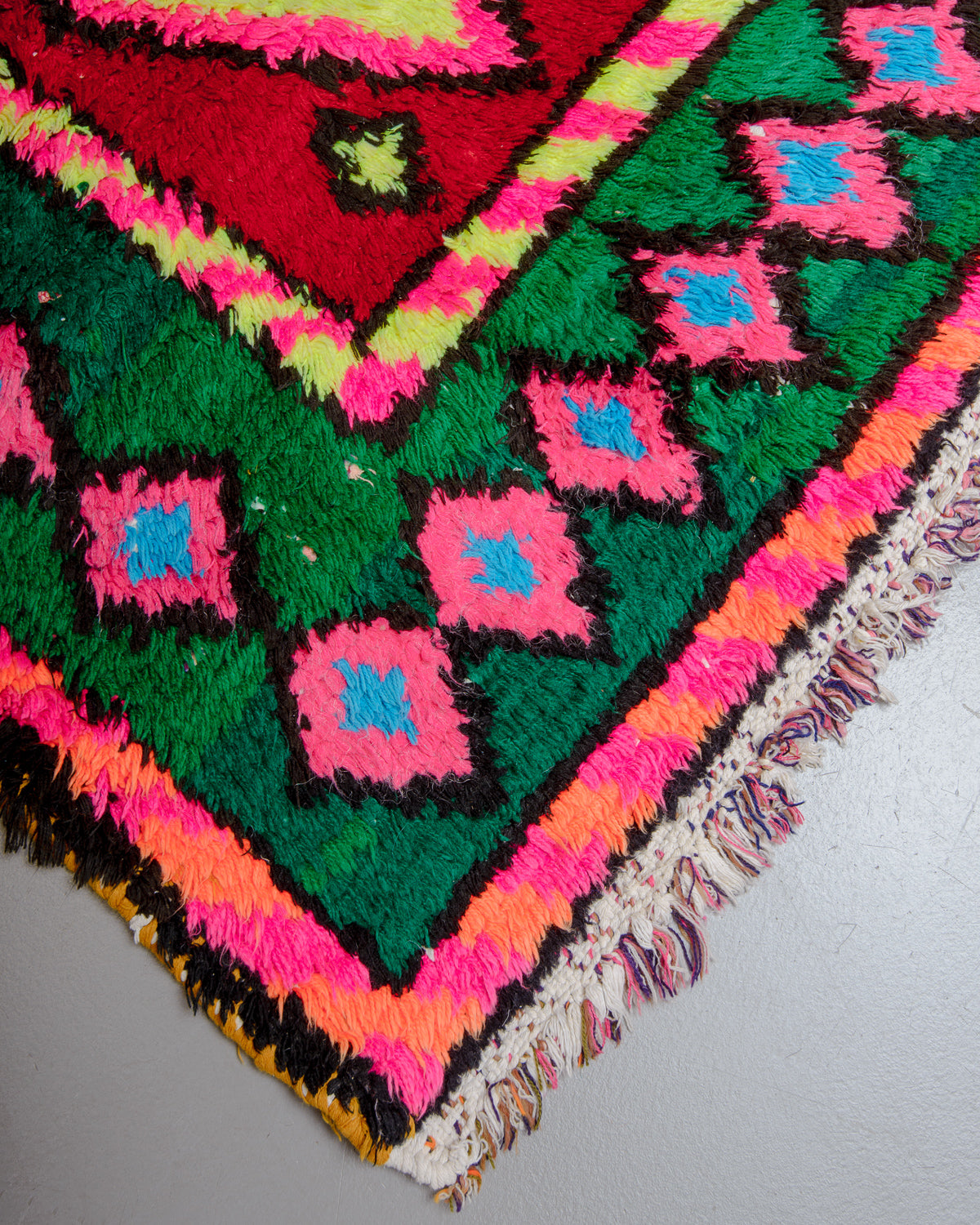 Corner of rug with neon pink, orange and yellow, green, blue and red.