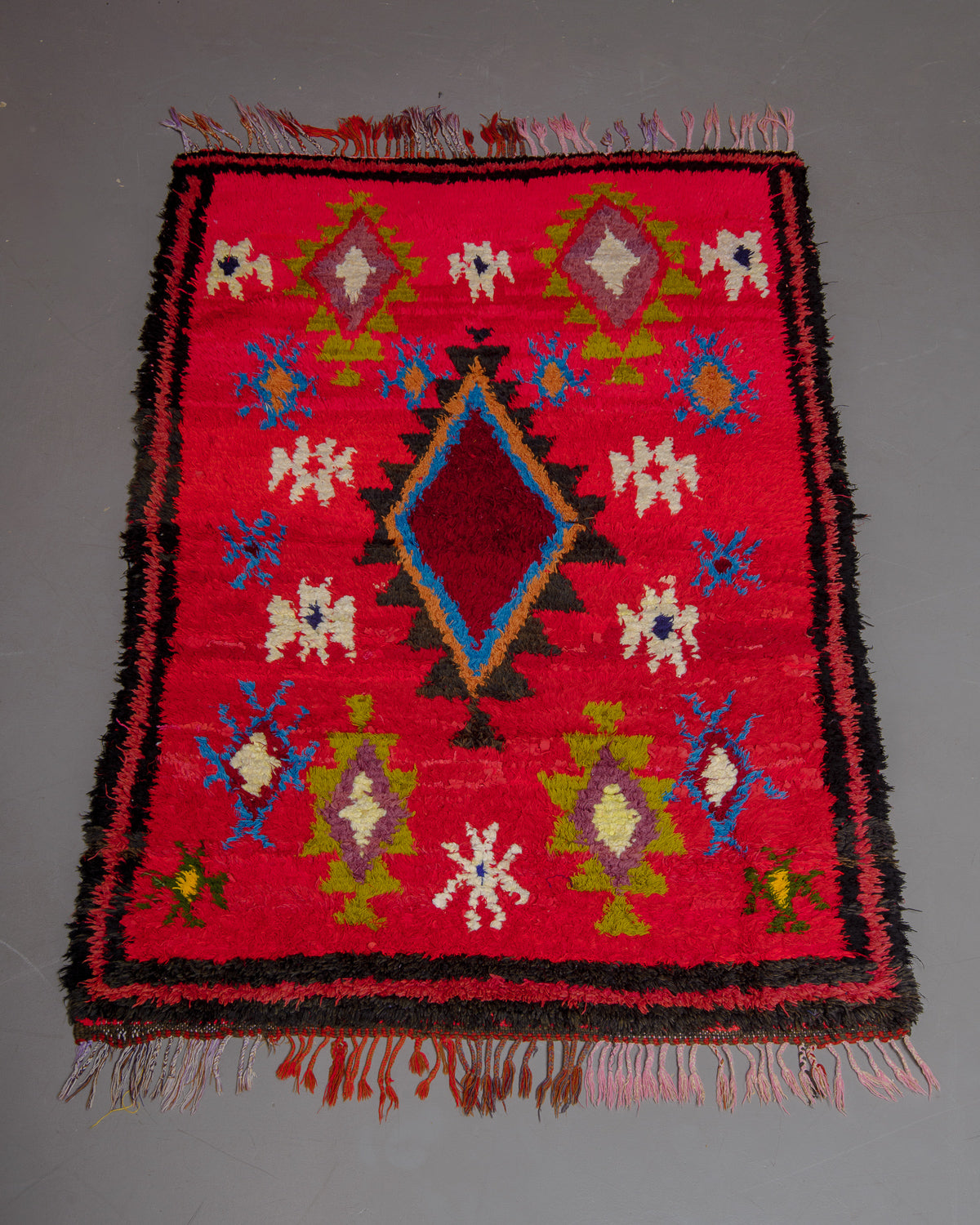 Vintage Berberlin boucherouite runner rug on grey floor in front of velvet curtain. 