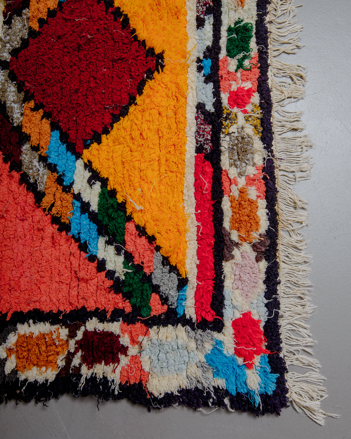 Corner of boucherouite rug with white cotton fringe.