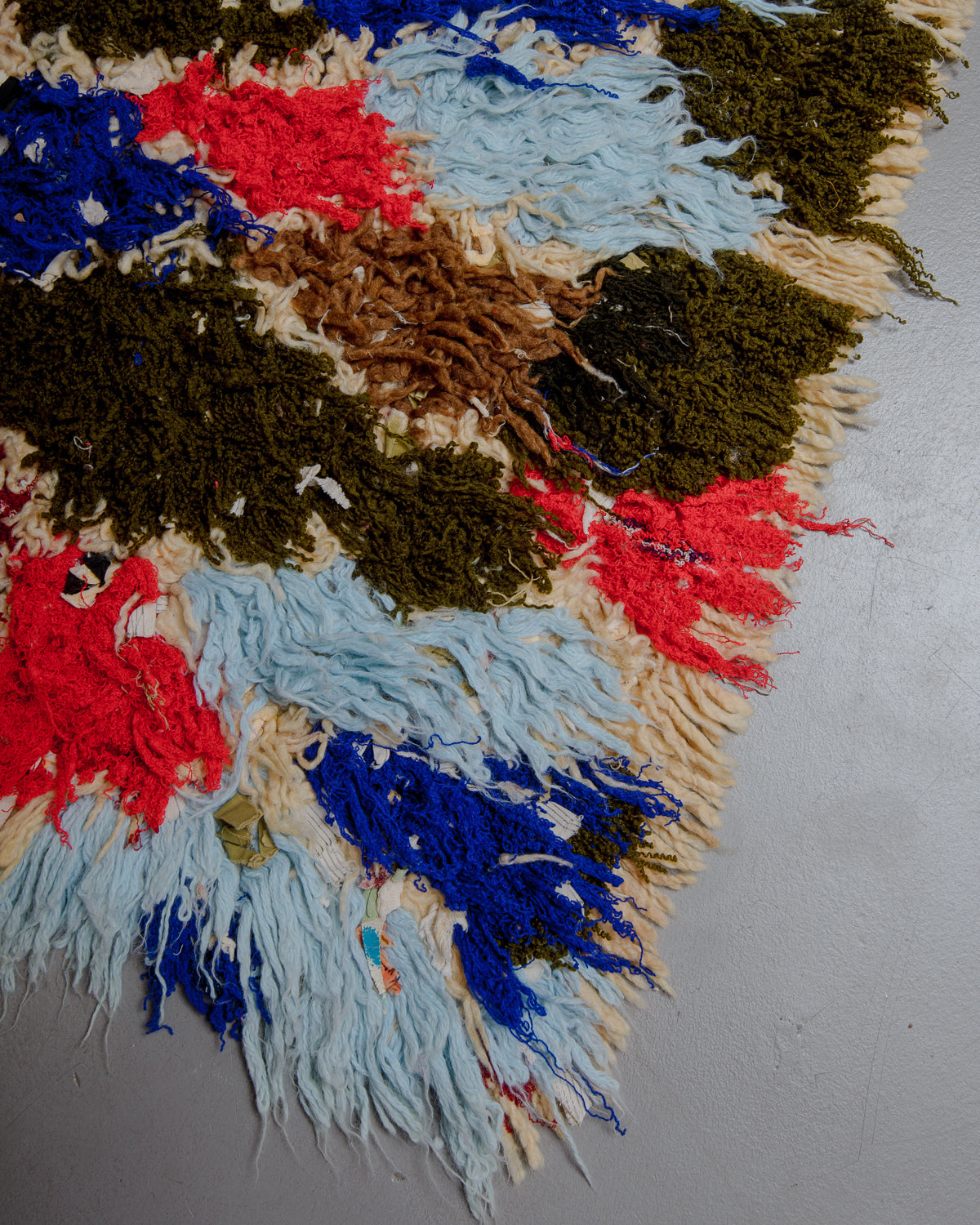 Corner of boucherouite rug with khaki, red, blue, brown and cream threads.